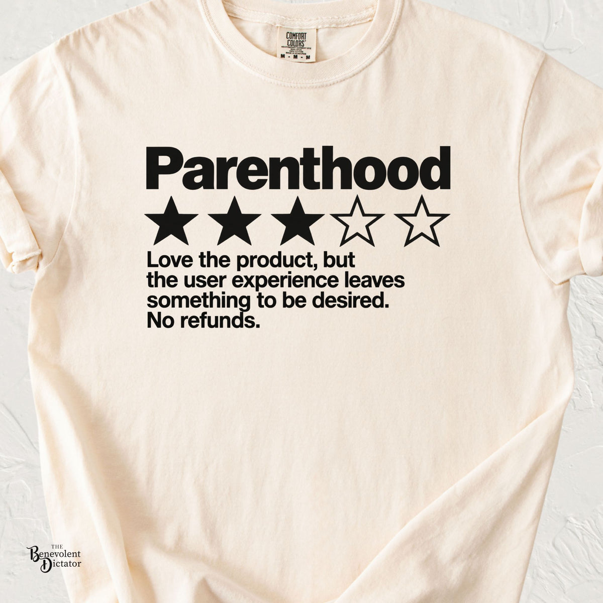 Ivory Comfort Colors t-shirt featuring a bold black Parenthood review graphic with three out of five stars and the text “Love the product, but the user experience leaves something to be desired. No refunds.”