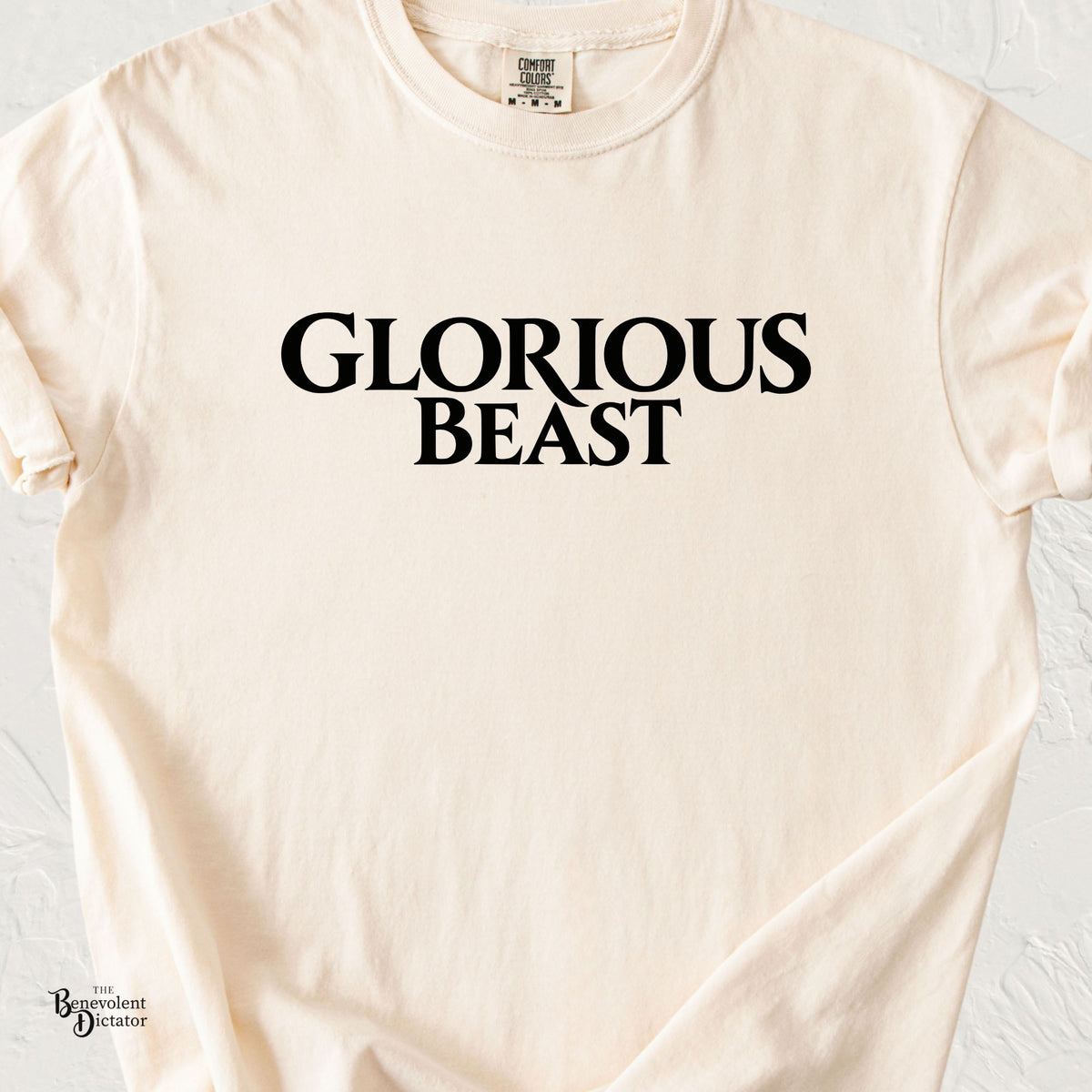 Ivory Comfort Colors t-shirt featuring bold black serif typography reading “Glorious Beast” in a minimalist, two-line design.