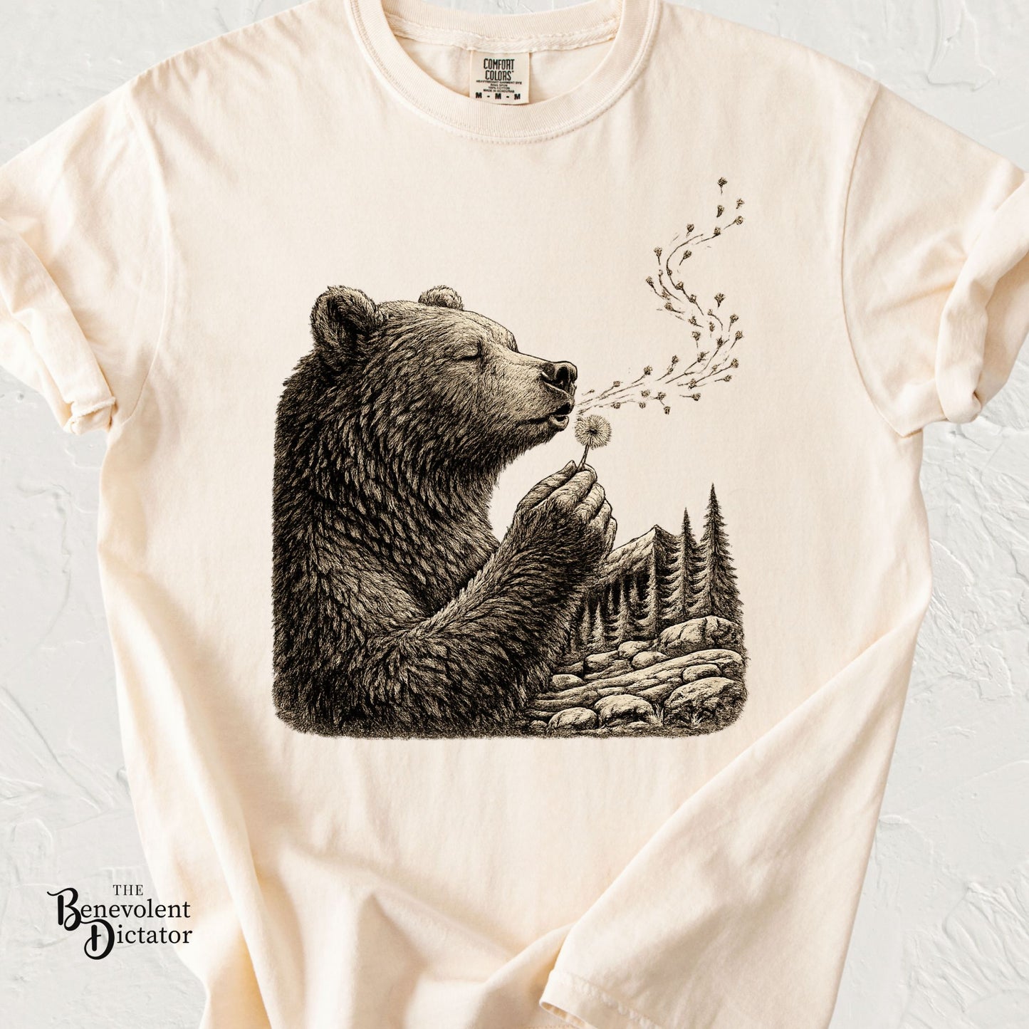 Vintage-style t-shirt featuring a detailed bear blowing a dandelion in a woodland landscape illustration.