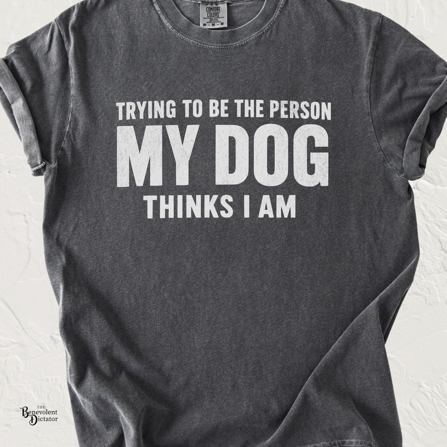 Typography t-shirt featuring the phrase Trying to Be the Person My Dog Thinks I Am in bold distressed lettering.