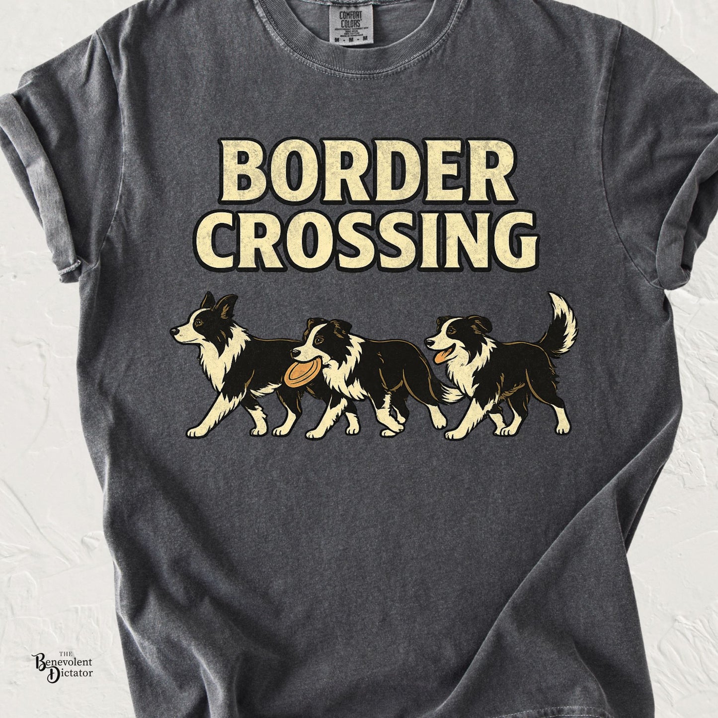 Comfort Colors pepper t-shirt featuring three vintage-style Border Collies crossing from left to right, one carrying a frisbee and another panting happily, beneath bold cream text reading "Border Crossing."