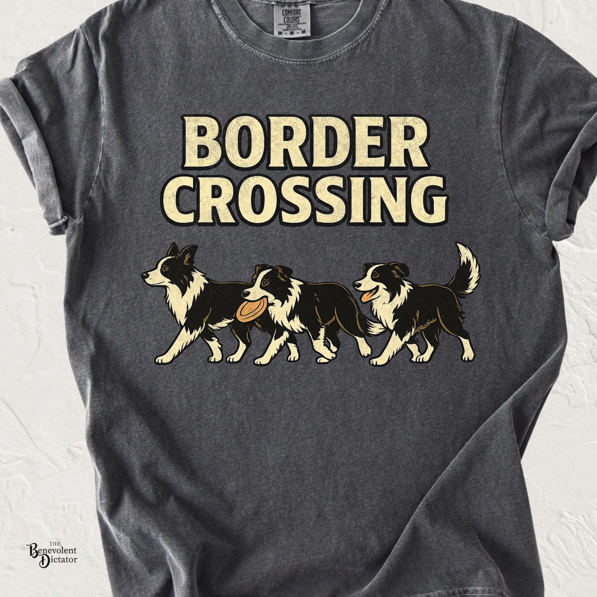 Comfort Colors pepper t-shirt featuring three vintage-style Border Collies crossing from left to right, one carrying a frisbee and another panting happily, beneath bold cream text reading "Border Crossing."
