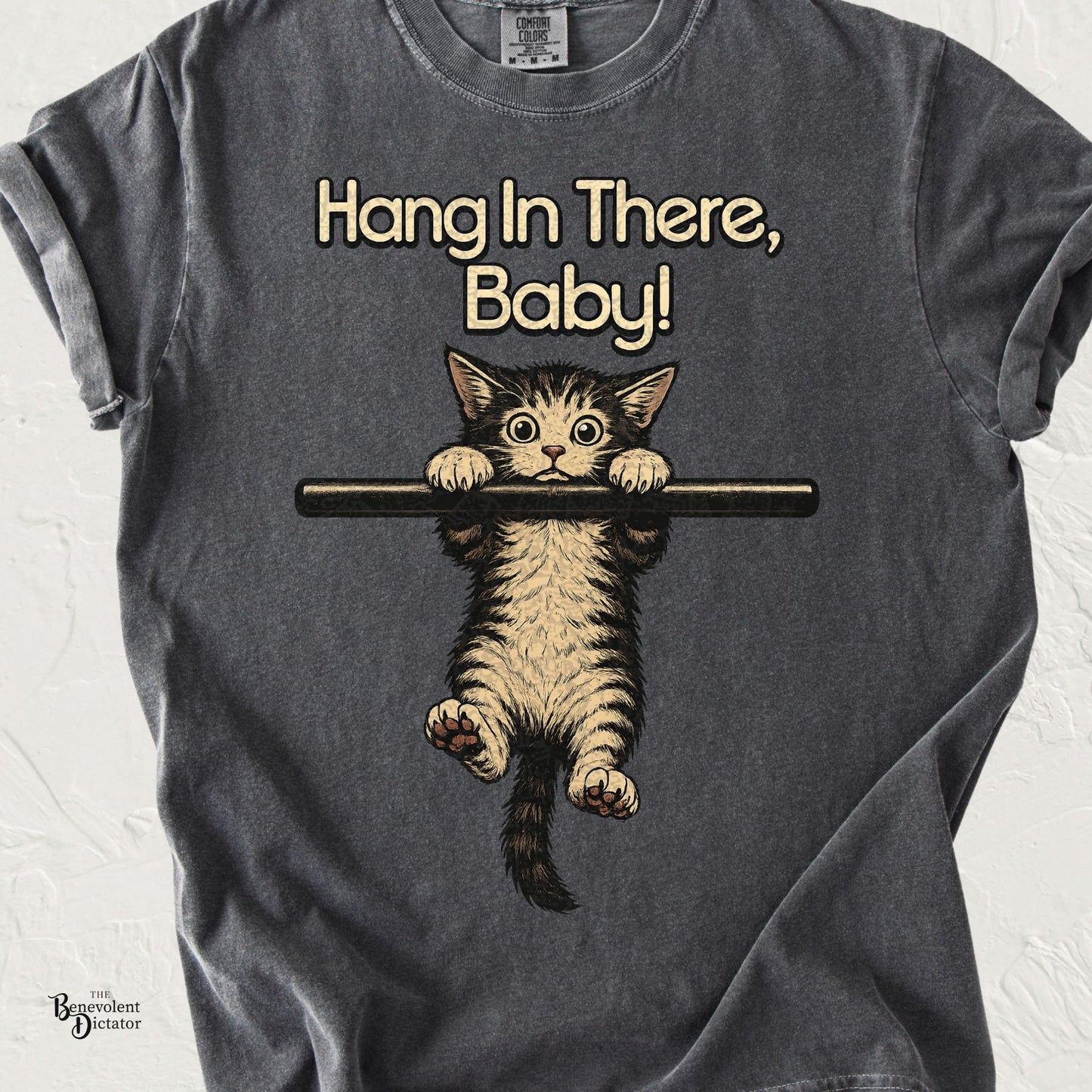 Comfort Colors pepper t-shirt featuring a vintage-style kitten hanging from a bar with the phrase "Hang In There, Baby!" inspired by the classic 1970s motivational poster.