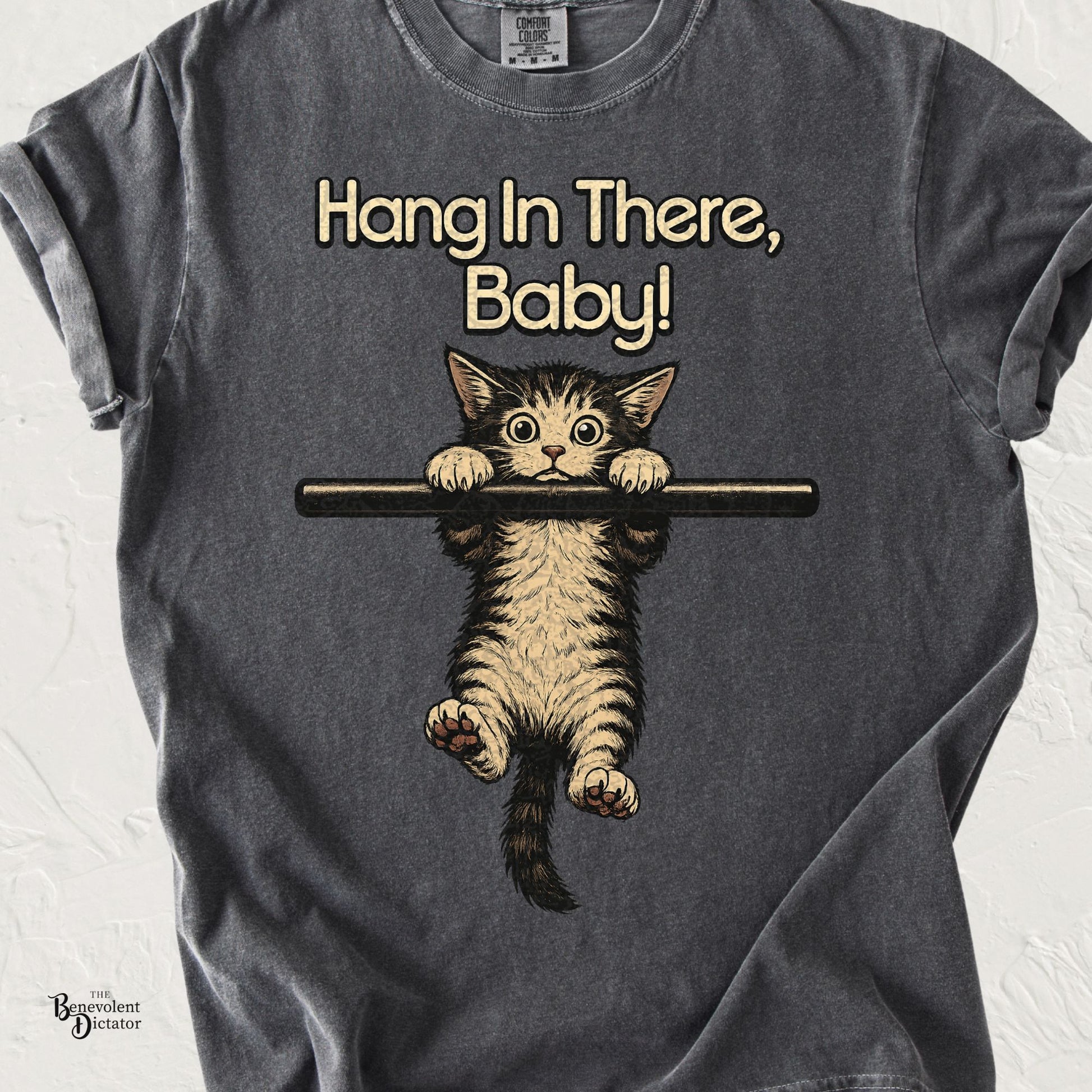Comfort Colors pepper t-shirt featuring a vintage-style kitten hanging from a bar with the phrase "Hang In There, Baby!" inspired by the classic 1970s motivational poster.