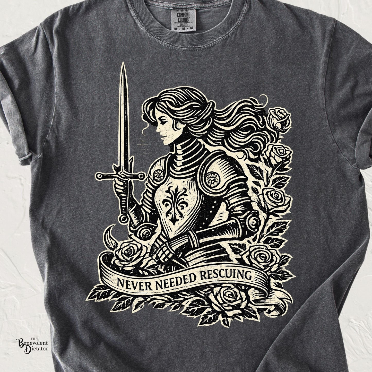 Vintage cream ink illustration of an armored female knight holding a sword, surrounded by roses with a banner reading Never Needed Rescuing on a pepper Comfort Colors t-shirt.