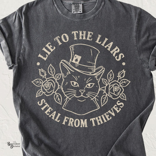 Vintage cream line art of a sly cat wearing a top hat surrounded by roses with the phrase Lie to the Liars, Steal from Thieves on a pepper Comfort Colors t-shirt.