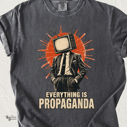Vintage graphic t-shirt featuring a suited man with a retro television for a head against an orange sunburst with the phrase “Everything Is Propaganda.”