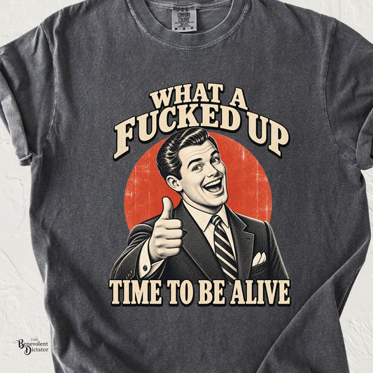 Pepper Comfort Colors t-shirt featuring a smiling retro man giving a thumbs-up with the phrase “What a Fucked Up Time to Be Alive” in distressed vintage typography.
