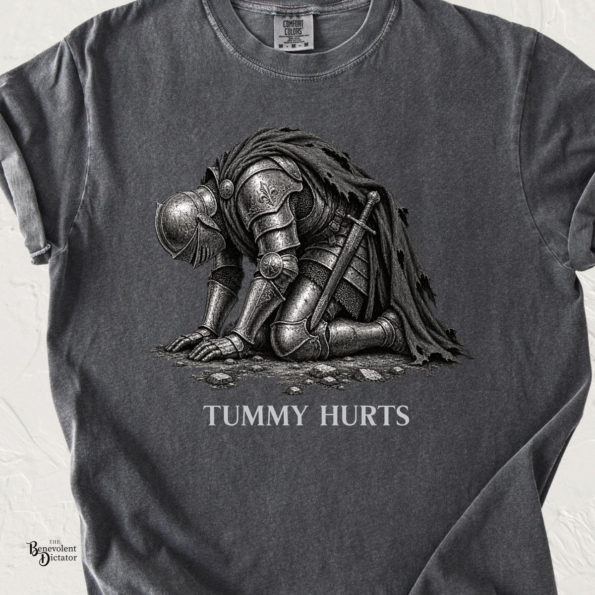 Pepper Comfort Colors t-shirt featuring a heavily armored medieval knight collapsed on his knees with the words “Tummy Hurts.”