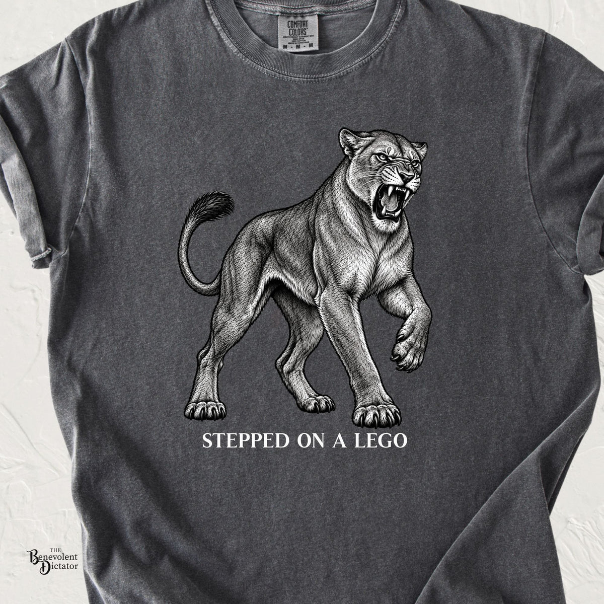 Pepper Comfort Colors t-shirt featuring an engraved snarling mountain lion lifting one paw above the words “Stepped on a Lego.”