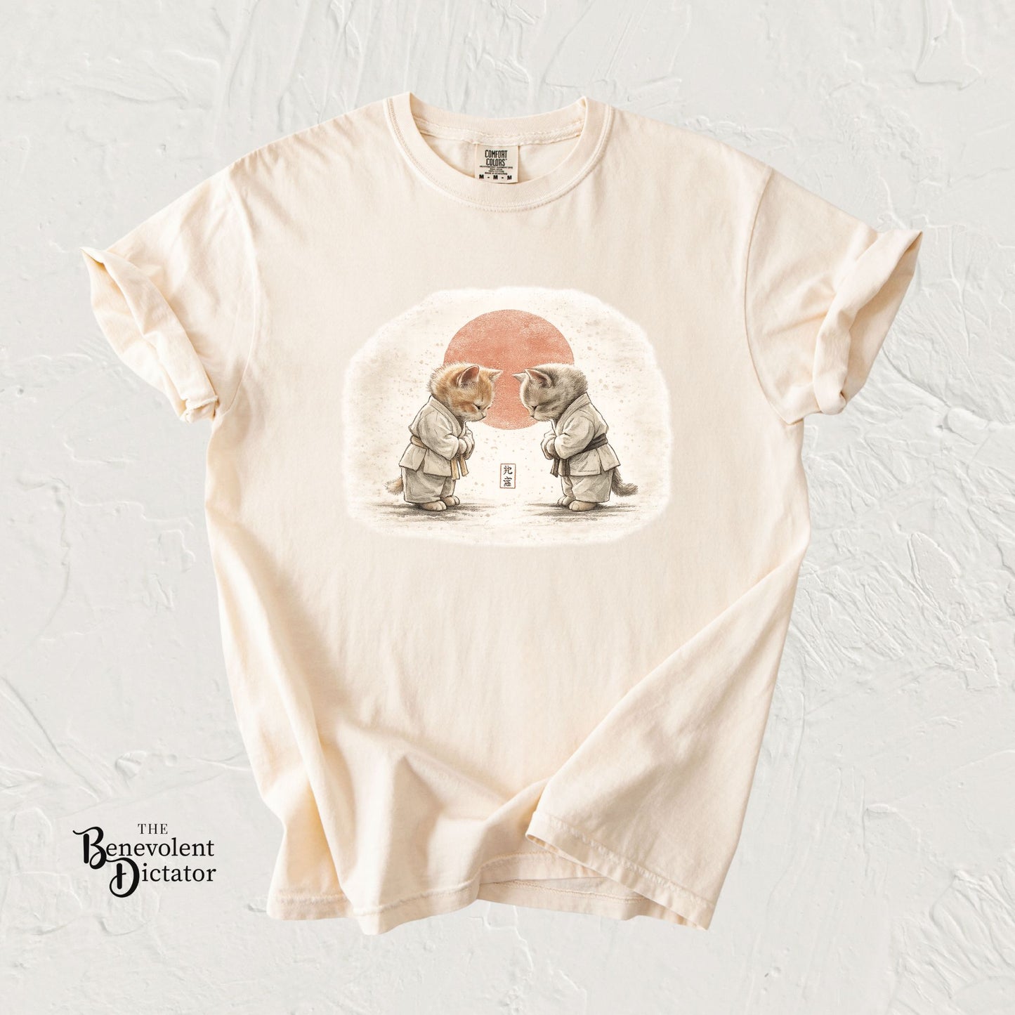 Beige t-shirt with a graphic of two elephants and a red sun on a textured white background.