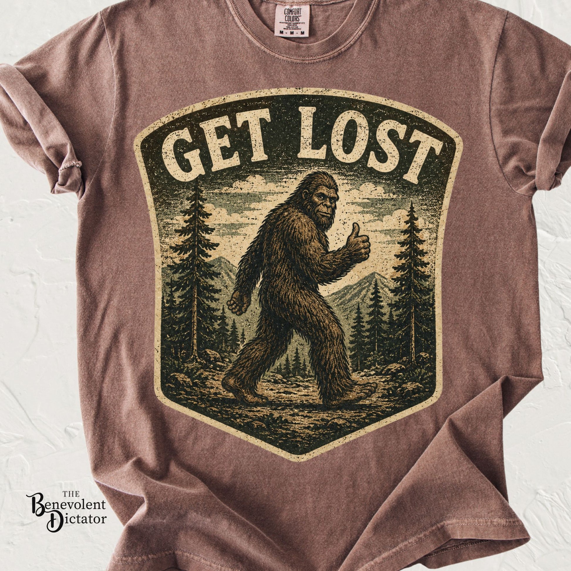 Vintage-style t-shirt featuring Bigfoot giving a thumbs up in a forest with the phrase Get Lost.