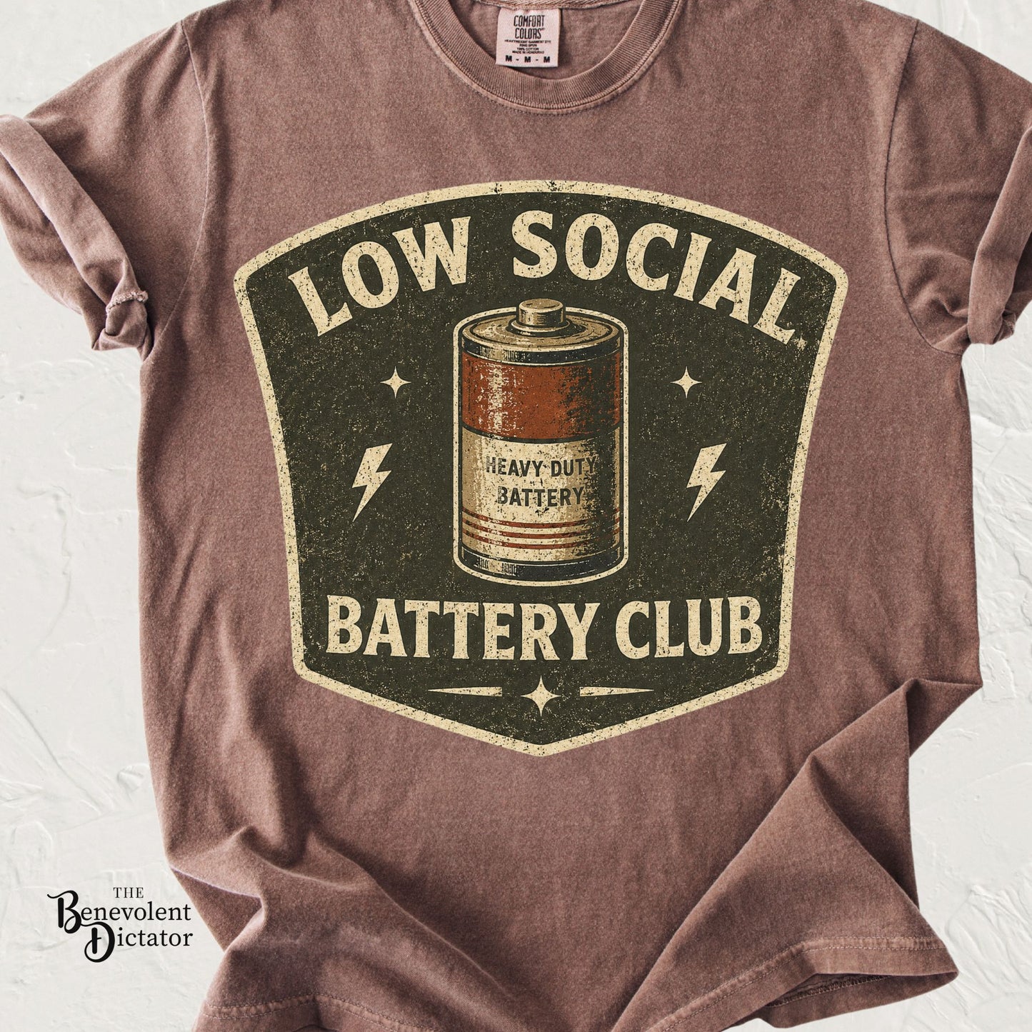 Vintage badge-style t-shirt featuring a low battery icon with the phrase Low Social Battery Club.
