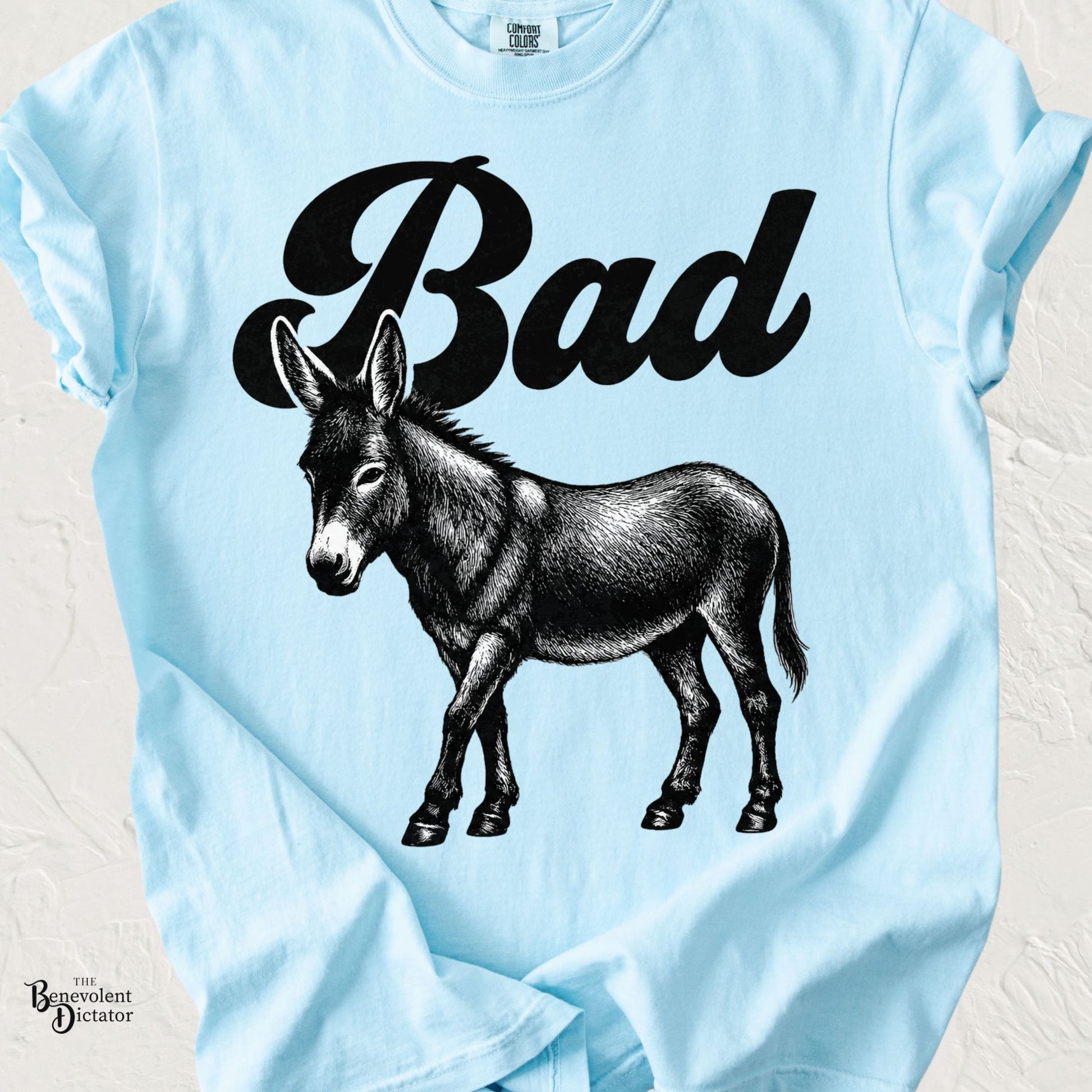 Vintage-style black and white donkey illustration beneath the word "Bad" in bold retro script on a Comfort Colors T-shirt.