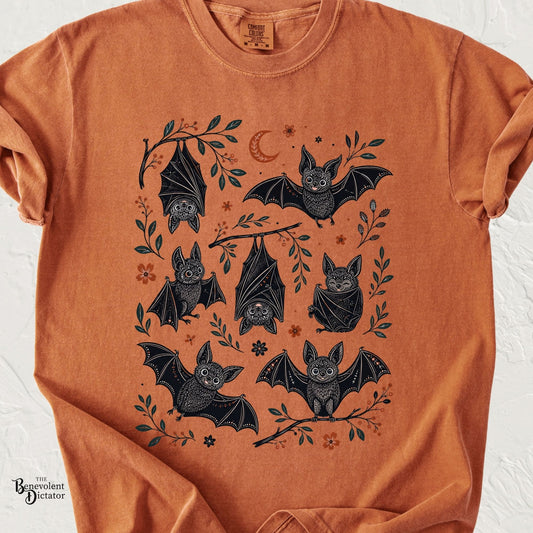 Yam Comfort Colors t-shirt featuring a whimsical collection of black bats flying, hanging upside down, and wrapped in their wings among leafy branches, flowers, and a crescent moon.