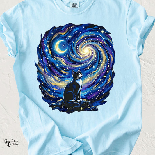 Light blue Comfort Colors t-shirt featuring a tuxedo cat sitting beneath a swirling starry night sky inspired by impressionist artwork with celestial stars and moon.