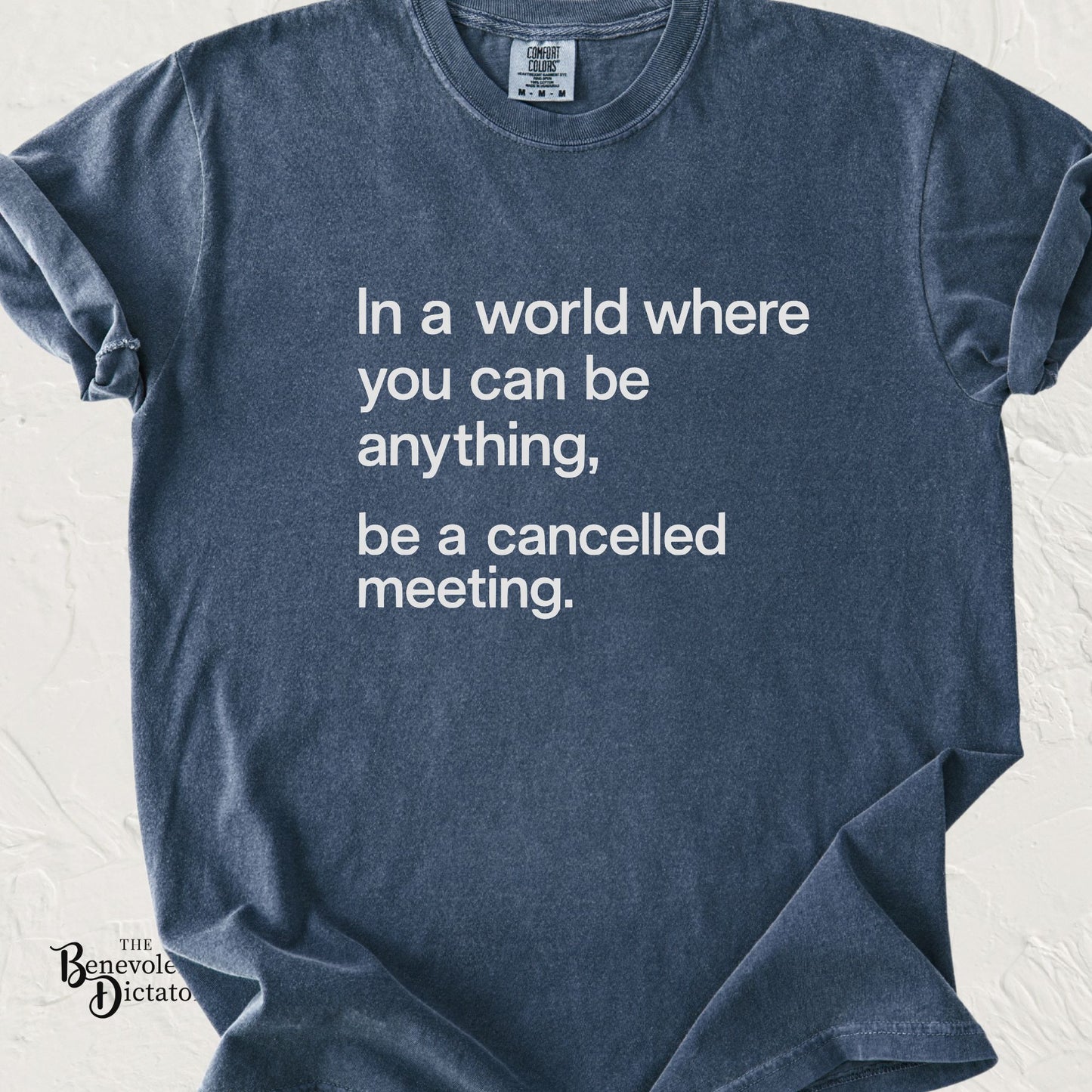 Blue Comfort Colors t-shirt featuring minimalist left-aligned white typography that reads "In a world where you can be anything, be a cancelled meeting."