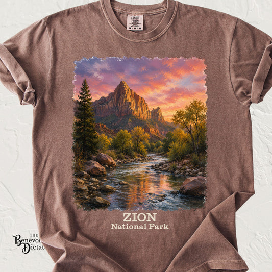 A brown short-sleeve t-shirt laid flat on a white textured background, featuring a large square graphic print of Zion National Park with a mountain sunset and a river, plus the text 'ZION National Park' on the front.