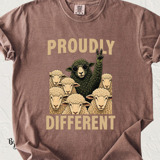 Espresso Comfort Colors t-shirt featuring a black sheep in sunglasses flashing a peace sign while surrounded by white sheep with the words “Proudly Different.”