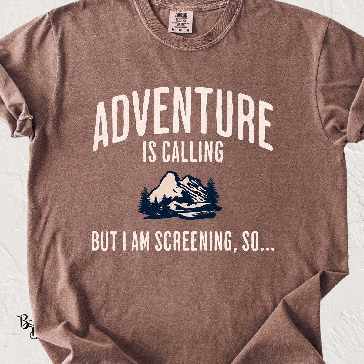 An espresso Comfort Colors short-sleeve t-shirt with a graphic print that reads 'ADVENTURE IS CALLING BUT I AM SCREENING, SO.