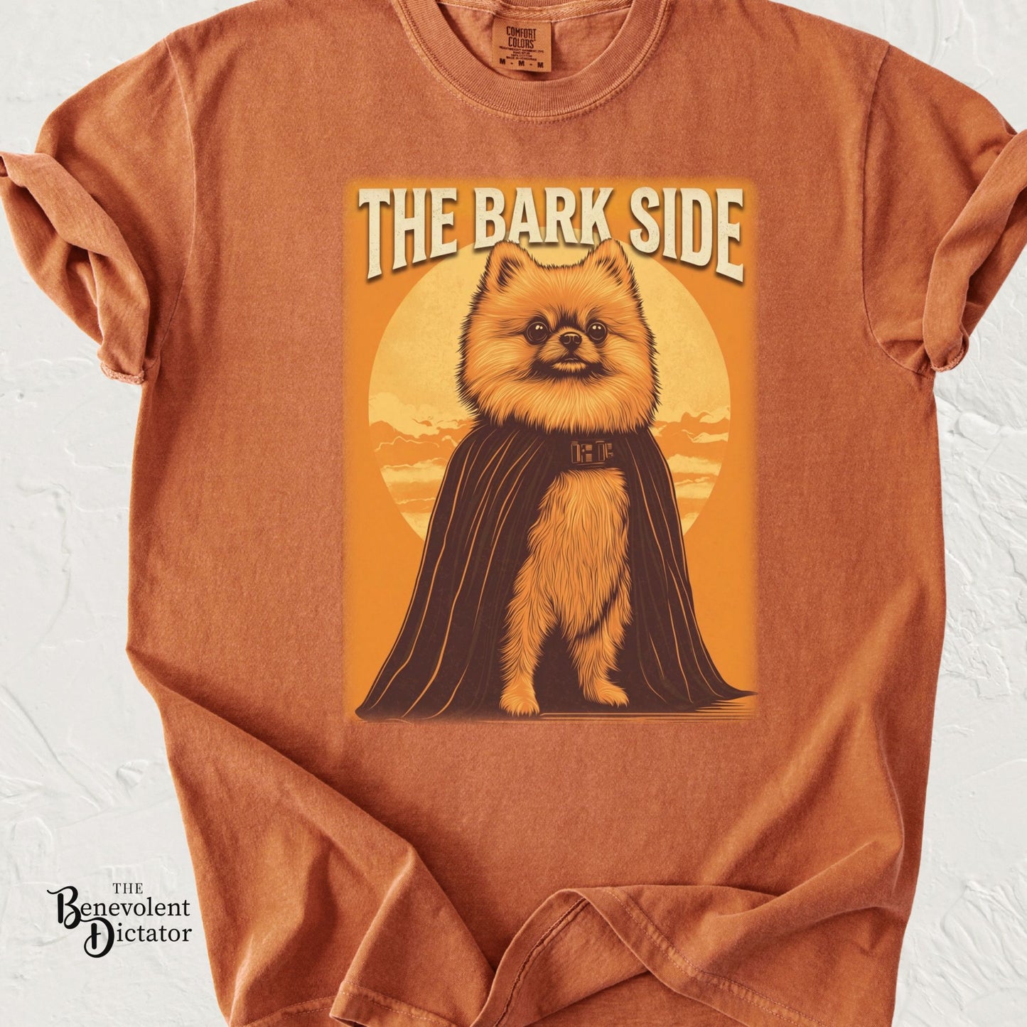 Funny graphic t-shirt featuring a Pomeranian in a dark cape with the phrase “The Bark Side.”